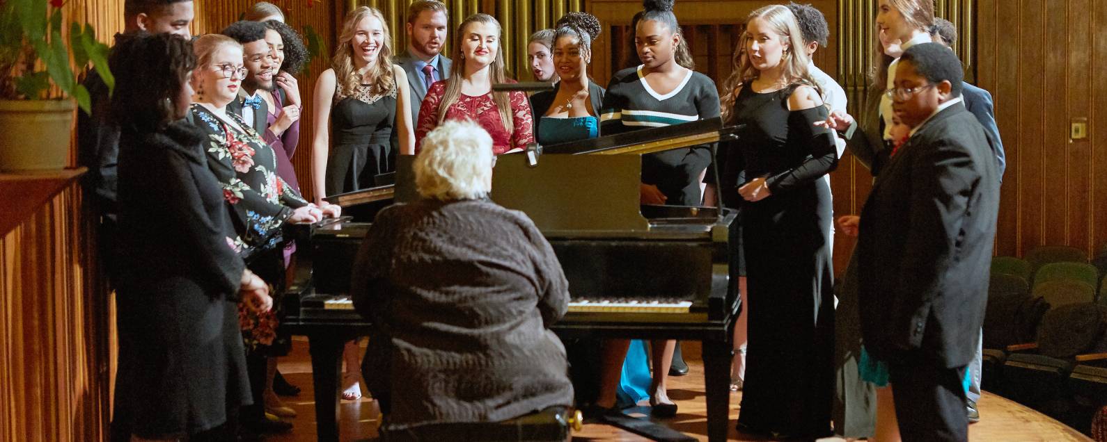A group of young Artists-in-Training gather around a piano at a recital.